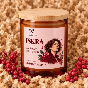 Świeca Iskra z różową etykietą na papierowym wypełniaczu, obok owoców różowego pieprzu.